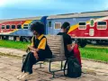 Deux personnes attendent sur un banc, un train coloré, un moyen de transport en Afrique, stationne derrière elles.