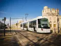 Le tramway moderne circule sur les rails à Avignon, passant devant des bâtiments historiques sous un ciel bleu éclatant.