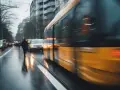 Un tram jaune file dans une rue mouillée, reflétant les lumières de la ville. Un bus Gien est visible au loin.