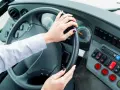 Vue de l'intérieur d'un bus, mains sur le volant. Le tableau de bord est visible, avec des boutons et des indicateurs. Le chauffeur est prêt à partir.
