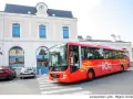Un bus rouge Lio, service public Occitanie, s'arrête devant une gare.