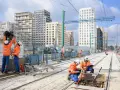 Des ouvriers travaillent sur de nouvelles infrastructures de tramway, avec des immeubles modernes en arrière-plan.