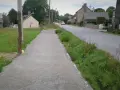 Un chemin de gravier longe une route de campagne bordée d'herbes folles. C'est un exemple de cheminement doux, invitant à la promenade paisible.