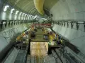 Intérieur d'un tunnel duplex en construction, avec des machines, des ouvriers et des tuyaux.