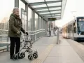 Une femme âgée avec un déambulateur attend le tram. Elle se prépare à monter, une leçon sur comment prendre le bus.