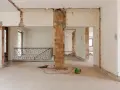 Intérieur en chantier, murs abattus, poutres apparentes. Les outils suggèrent une rénovation, pas une simple réhabilitation.