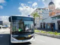 Un bus Esterel côte d'Azur circule dans une ville ensoleillée, près d'un port et d'une église.
