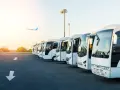 Une flotte de bus blancs alignés, prêts à transporter des passagers. L'avion au loin suggère la capacité d'un bus à relier les gens à leurs destinations.