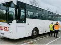 Un bus blanc "Véhicule École" est garé. Deux instructeurs, un homme et une femme, portent des gilets de haute visibilité.