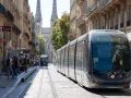 Un tramway moderne circule dans une rue pavée bordée de bâtiments anciens, témoignant du projet tramway urbain.