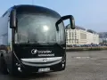 Autocar noir Transdev Normandie garé sur un quai, avec des bâtiments en arrière-plan.