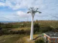 Un pylône blanc massif soutient un téléphérique urbain au-dessus d'une ville et d'une colline boisée.