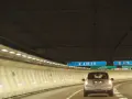 Voiture dans un tunnel éclairé, direction A10-A6 et A13. Un panneau indique Créteil et Versailles. Passage d'un duplex péage.