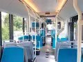 Intérieur d'un bus IDFM moderne avec des sièges bleus et gris, des barres de maintien et de grandes fenêtres donnant sur la verdure.