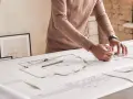 Un architecte dessine des plans détaillés, traçant des lignes précises pour un projet. Il y a plu trappes sur la table.
