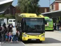Des bus jaunes et verts attendent des passagers. Une affiche sur le bus vert mentionne "100% GRATUIT", illustrant la gratuité des transports en commun.