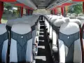 Intérieur d'un tour bus avec des sièges confortables et des rideaux rouges.