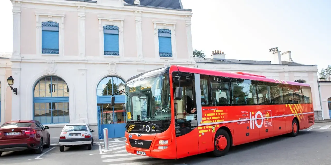 Un bus rouge Lio, service public Occitanie, s'arrête devant une gare.