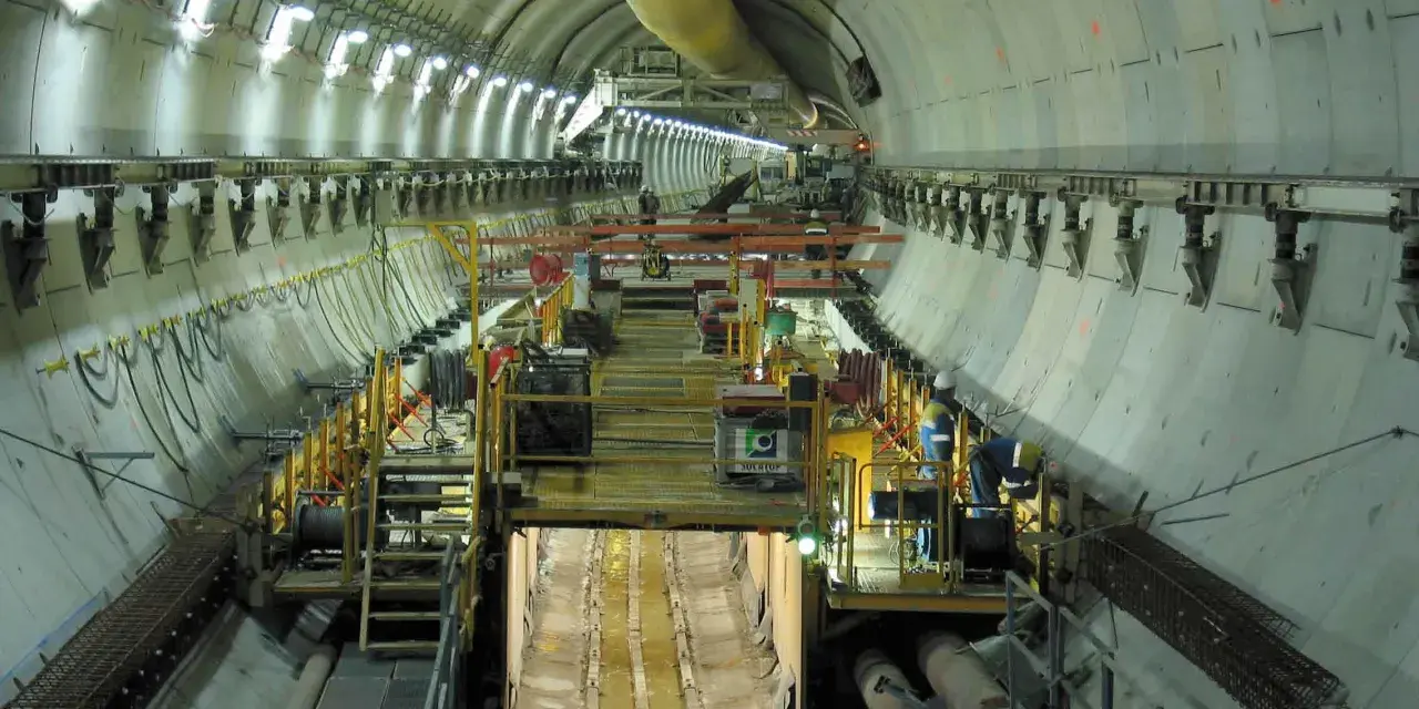 Intérieur d'un tunnel duplex en construction, avec des machines, des ouvriers et des tuyaux.