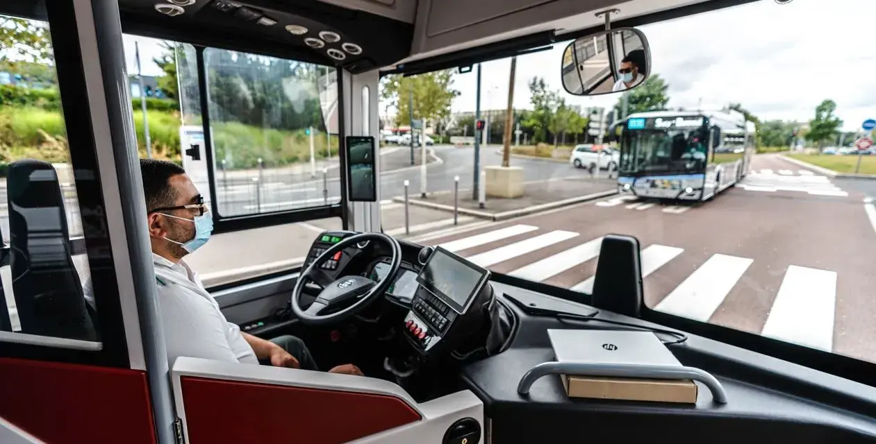 Vue de l'intérieur d'un bus RATP, le conducteur porte un masque. Un autre bus approche au loin.