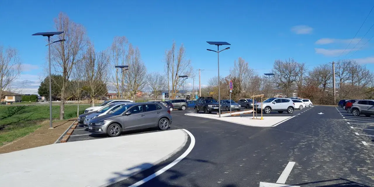 Stationnement de voitures dans une aire covoiturage Toulouse, éclairée par des lampadaires solaires sous un ciel bleu.