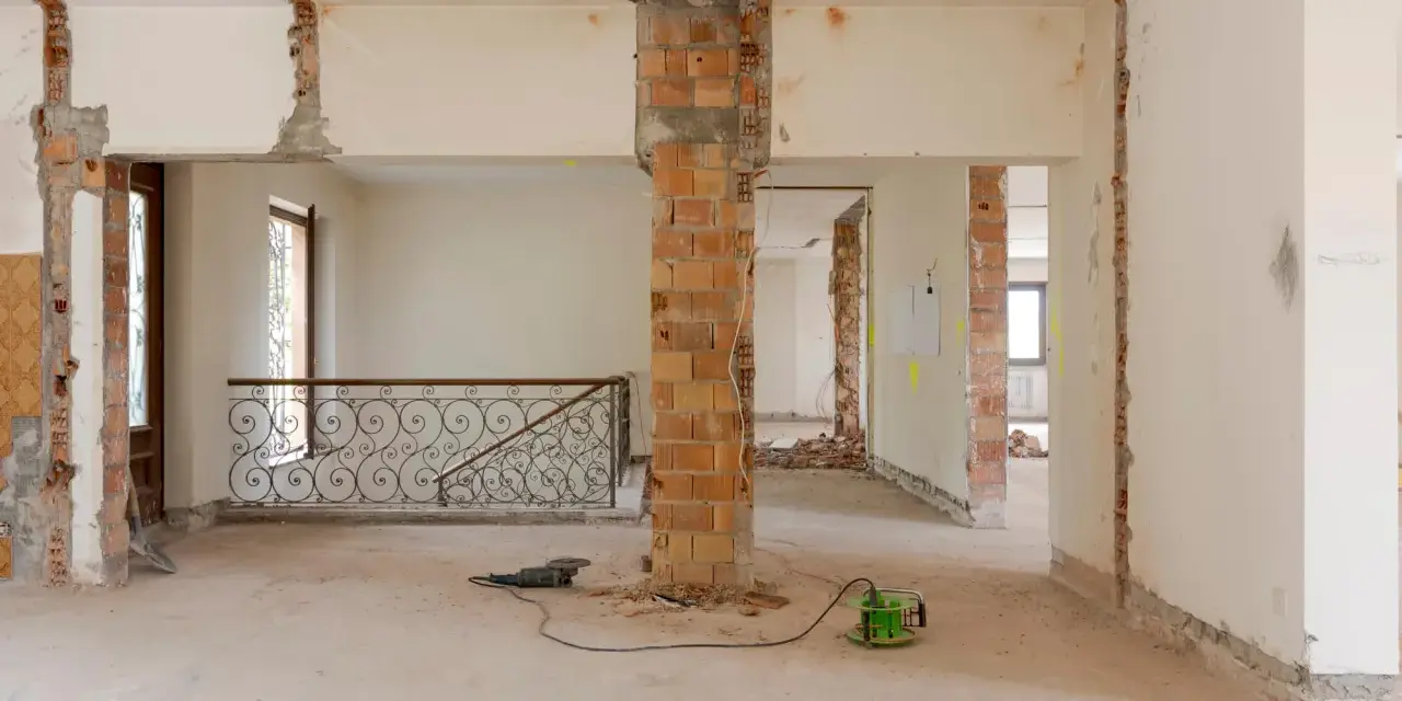 Intérieur en chantier, murs abattus, poutres apparentes. Les outils suggèrent une rénovation, pas une simple réhabilitation.