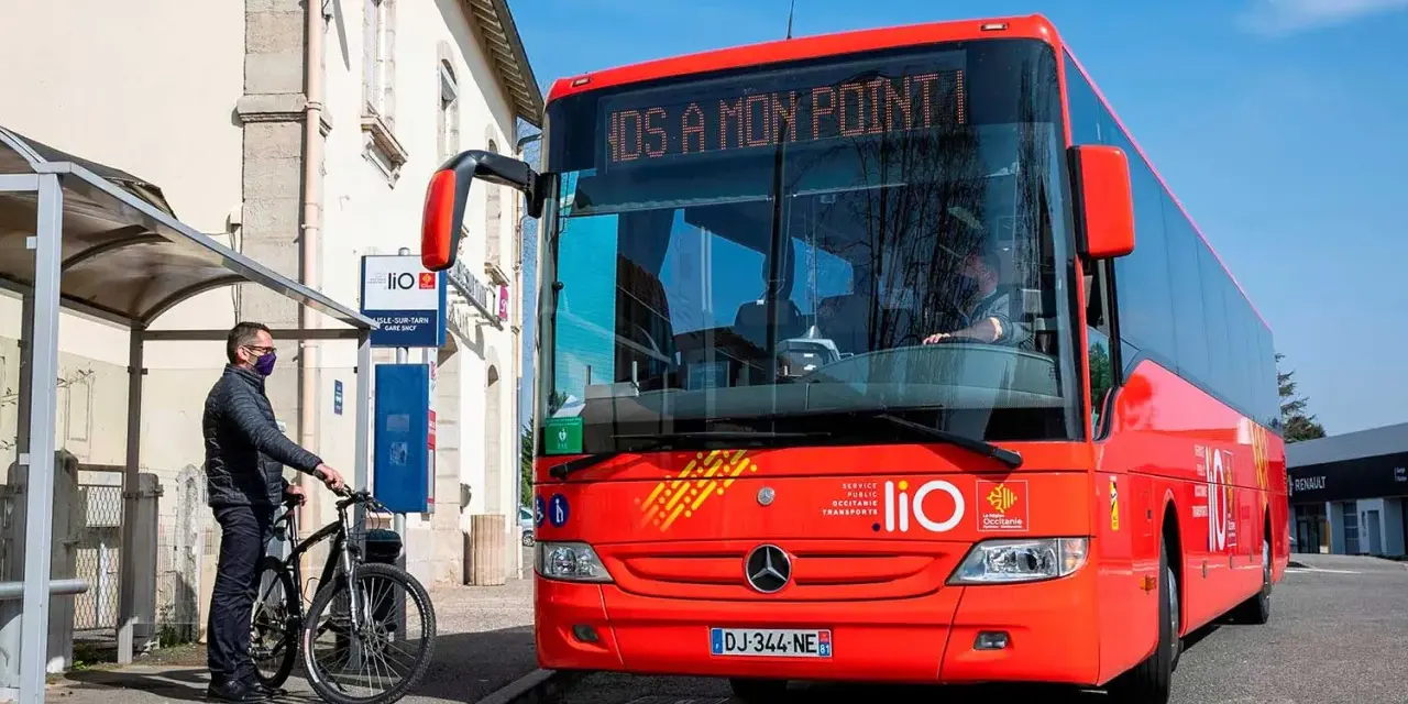 Un homme attend un bus LIO rouge à un arrêt, prêt à monter avec son vélo. Ce bus dessert les lignes comme Graulhet Gaillac.