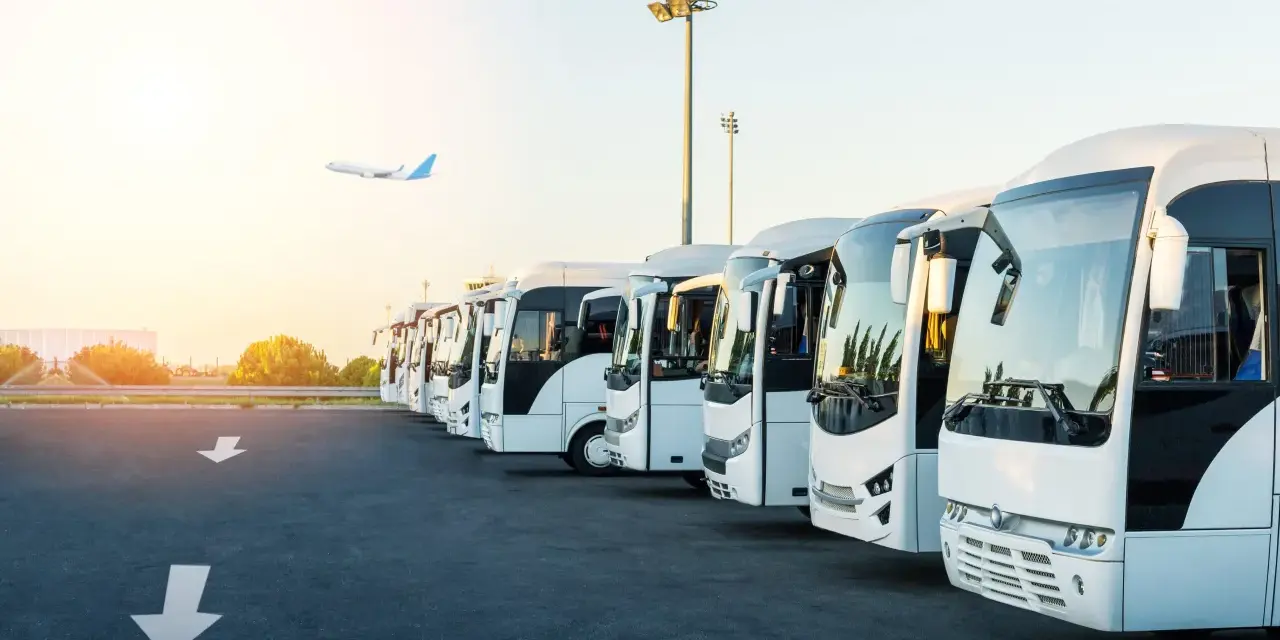 Une flotte de bus blancs alignés, prêts à transporter des passagers. L'avion au loin suggère la capacité d'un bus à relier les gens à leurs destinations.