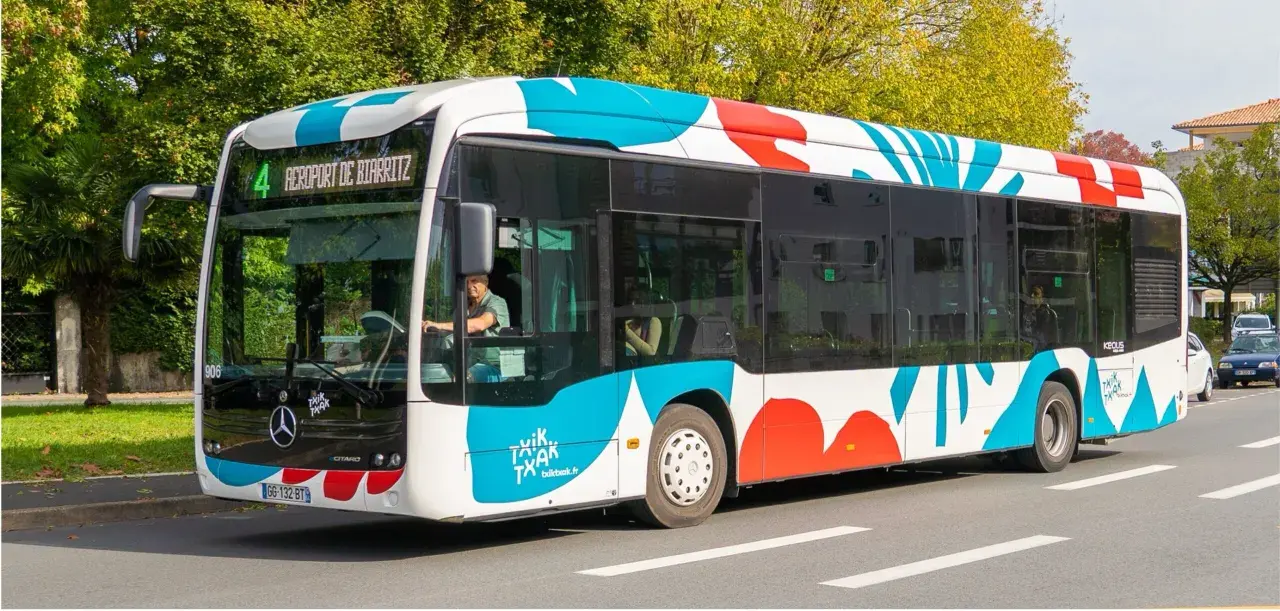 Bus txiktxak Bayonne, ligne 4, direction Aéroport de Biarritz, avec un motif coloré bleu et rouge sur fond blanc.