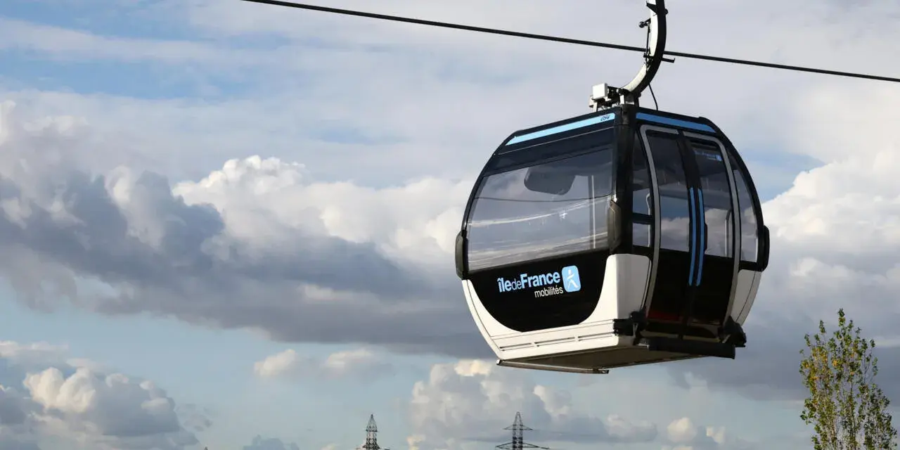 Cabine de téléphérique urbain en France, survolant un paysage urbain sous un ciel nuageux.