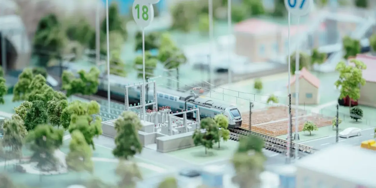 Maquette ferroviaire avec un train, des arbres et des maisons. Des panneaux indiquent des dates, peut-être pour un projet mobco 2026.