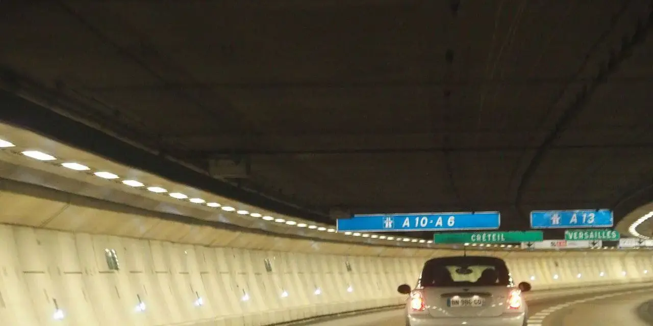 Voiture dans un tunnel éclairé, direction A10-A6 et A13. Un panneau indique Créteil et Versailles. Passage d'un duplex péage.