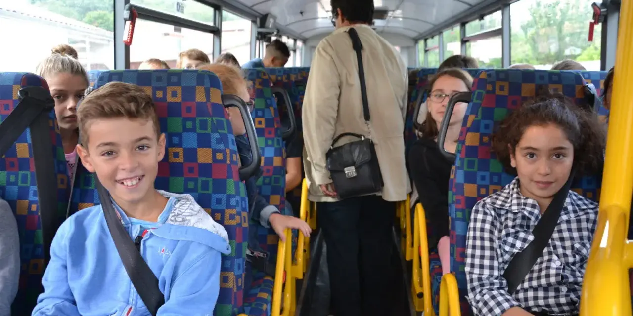 Des enfants souriants et une adulte voyagent dans un autobus scolaire aux sièges colorés.