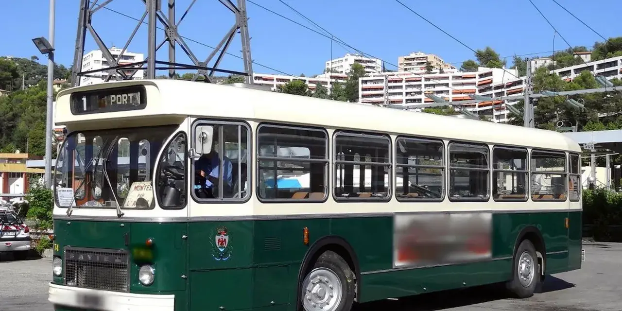 Un bus Saviem SC10, vert et crème, circule sous un ciel bleu. Il est stationné sur un parking, avec des immeubles en arrière-plan.