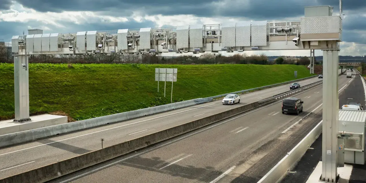 Portique de péage urbain sur une autoroute, avec des voitures passant sous les caméras.