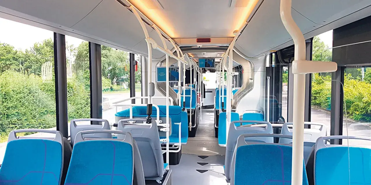 Intérieur d'un bus IDFM moderne avec des sièges bleus et gris, des barres de maintien et de grandes fenêtres donnant sur la verdure.