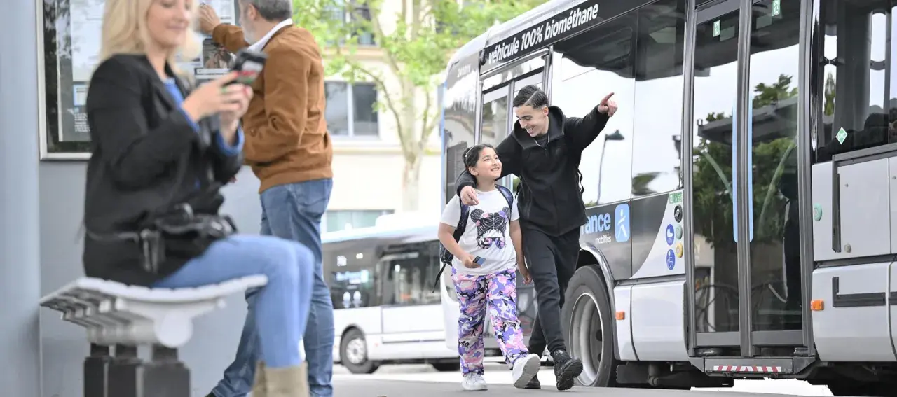Un jeune homme et une fillette souriants marchent près d'un bus Transdev à Blois.