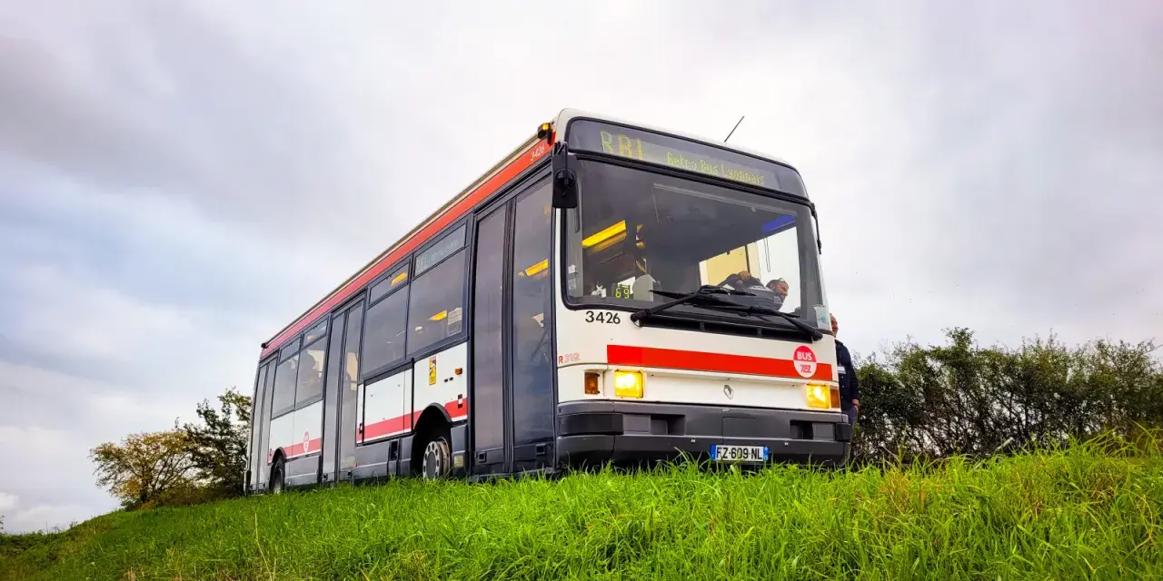 Un bus Renault R312 blanc et rouge, immatriculé FZ-609-NL, roule sur une colline herbeuse sous un ciel couvert.