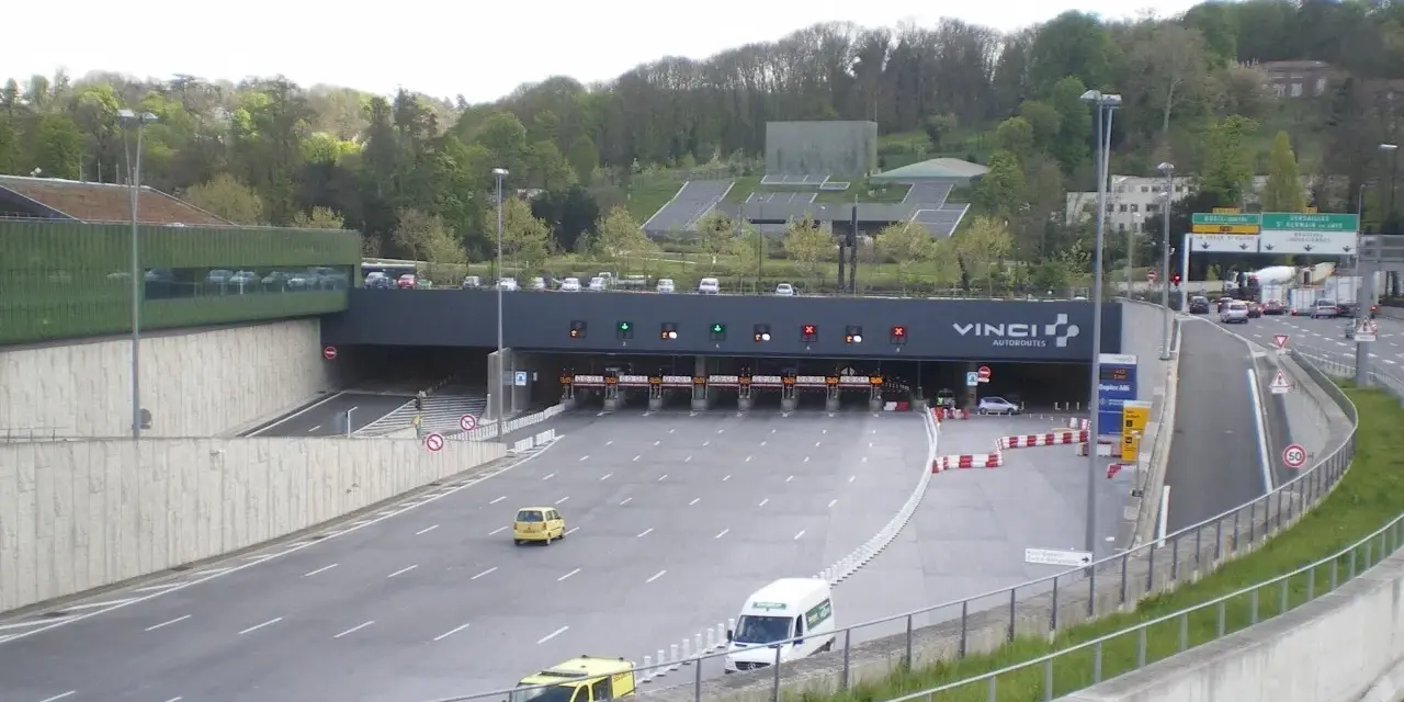 Entrée d'un **duplex autoroute** Vinci. Des voitures et des camions passent sous des portiques de péage.