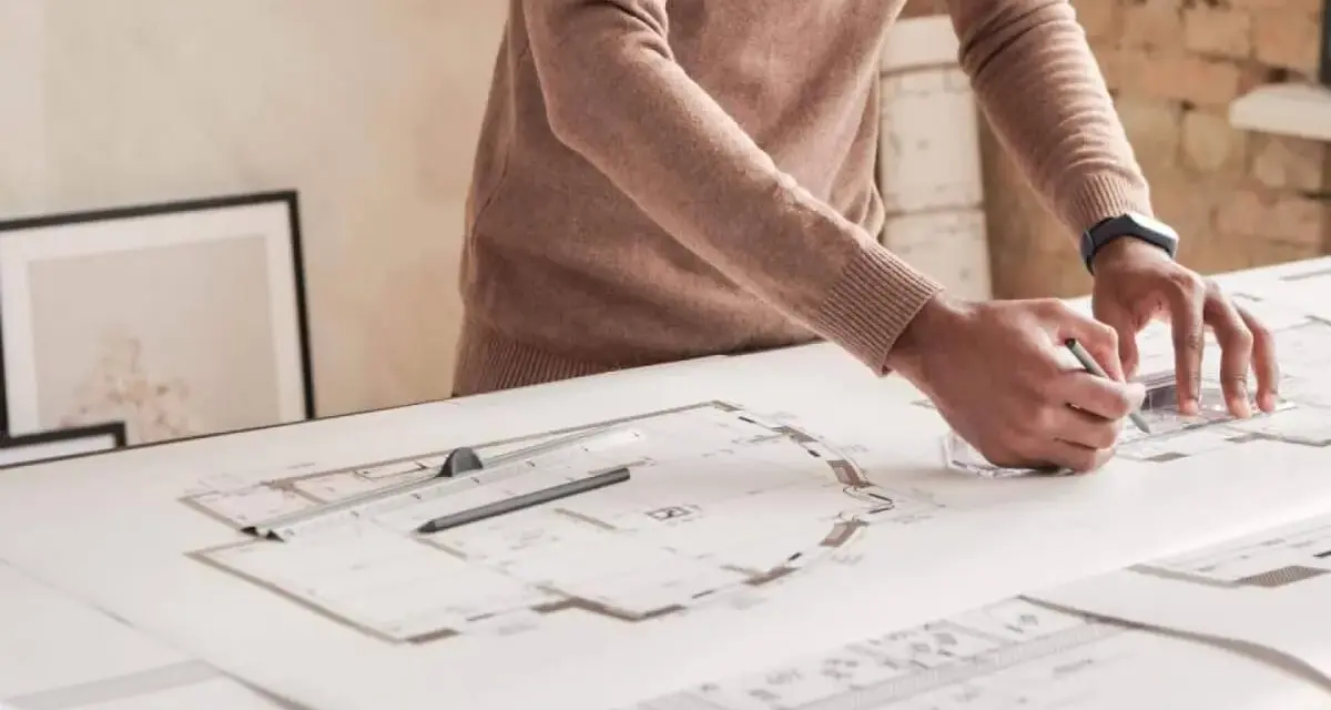 Un architecte dessine des plans détaillés, traçant des lignes précises pour un projet. Il y a plu trappes sur la table.