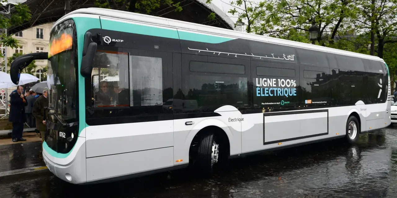 Un bus RATP bleu et blanc, "LIGNE 100% ÉLECTRIQUE", roule sur une chaussée mouillée.