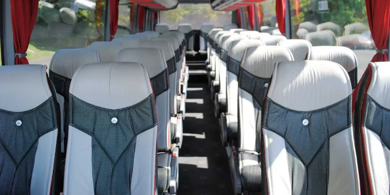 Intérieur d'un tour bus avec des sièges confortables et des rideaux rouges.