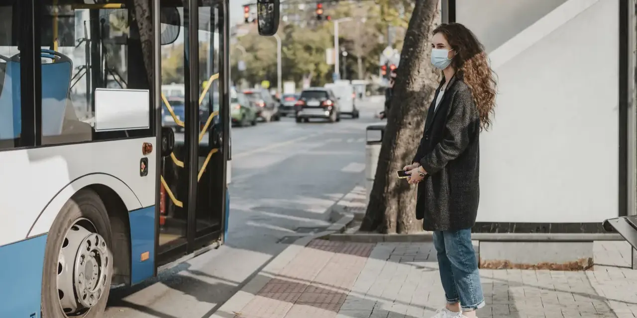 Une jeune femme avec un masque attend le bus, un moyen de déplacement pratique en ville.