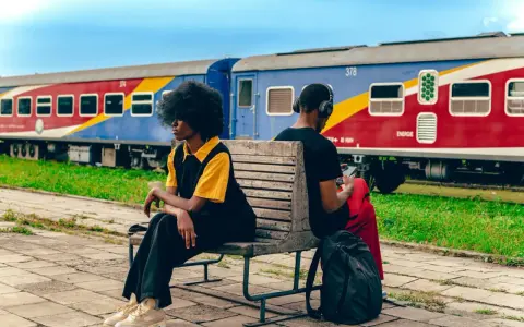 Deux personnes attendent sur un banc, un train coloré, un moyen de transport en Afrique, stationne derrière elles.