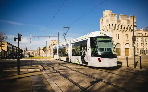 Le tramway moderne circule sur les rails à Avignon, passant devant des bâtiments historiques sous un ciel bleu éclatant.