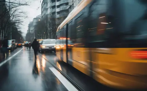 Un tram jaune file dans une rue mouillée, reflétant les lumières de la ville. Un bus Gien est visible au loin.