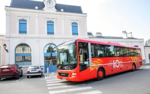 Un bus rouge Lio, service public Occitanie, s'arrête devant une gare.