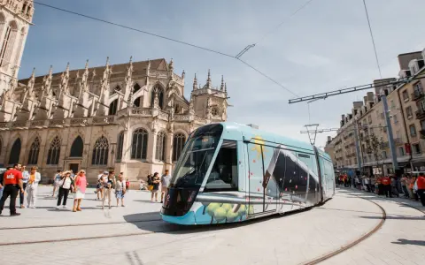 Un tram **Keolis Vélizy** décoré circule devant une cathédrale gothique. Des passants attendent sur le quai.