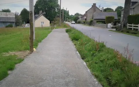 Un chemin de gravier longe une route de campagne bordée d'herbes folles. C'est un exemple de cheminement doux, invitant à la promenade paisible.