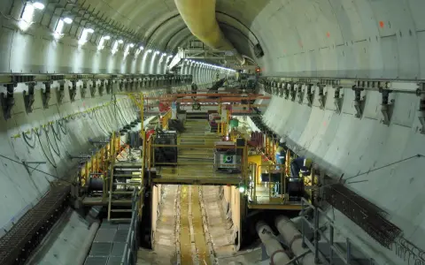 Intérieur d'un tunnel duplex en construction, avec des machines, des ouvriers et des tuyaux.
